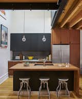 The kitchen features Schoolhouse Electric & Supply Co. pendant lights and Crate and Barrel stools. The woodblock island's leaf, at the far right, can lift upwards to expand the table when work or hosting demands it. The faucet is from KWC.