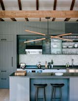 In New York about two hours north of New York City, architecture and interiors firm BarlisWedlick created an eclectic compound designed to suit a client with an idiosyncratic wish list. In the kitchen, a custom Stickbulb LED lamp hangs above a kitchen island topped by concrete from Get Real Surfaces. The cabinets and island feature a modern version of a traditional board and batten siding that are given an even more contemporary feel with the concrete countertop.