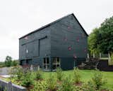 Two hours north of New York City, an unusual barn emerges from a hill just off a country road. Its black siding and bright-red window frames hint at the imaginative playground inside. This space, with its rope-railed catwalk and indoor tent, is just one element of the multifaceted getaway architecture and design firm BarlisWedlick Architects designed for fund manager Ian Hague.