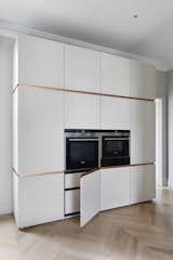 The opposite wall of the kitchen features built-in Siemens appliances and concealed storage. The custom INTERIOR-iD cabinets feature mitered doors, and brass trim, which passes fluidly around the edge of the doors, terminating at the back wall.