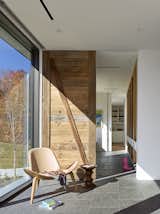The front entry opens into a mud room. Each family member has their own cubby for storing shoes, coats, and backpacks. The wood sliding door, seen here, was built from reclaimed barn board. In front of it stands a Chair CH07 by Hans Wegner for Carl Hansen & Son Shell and Eames Walnut stool from Herman Miller.