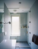 Triple-glazed, frosted windows emit soft, filtered light against pale gray and blue surfaces inthe master bathroom. Lucian Field matte-glass and Lucian Mosaics penny round tiles, both by Ann Sacks, line the floor and walls.