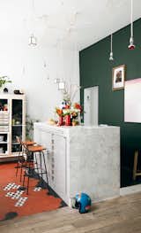 Aumas designed the kitchen island, which is covered in marble tiles from Carrelages du Marais—the geometric floor tiles are from the same place—and strung the matrix of lights up above it. The barstools by Charlotte Perriand were discovered in a vintage store in Antwerp, Belgium. The green wall is covered in paint from Emery &amp; Cie.  Photo 4 of 13 in Enter the Parisian Flat of a Globetrotting Artistic Director