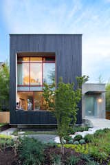 Front Yard, Trees, Walkways, Exterior, Wood, and House The street-facing facade leans into the landscape with a three-foot-deep cantilever and toward a pathway of hexagonal concrete pavers.  Exterior Walkways Front Yard Photos from A Wild Garden Leaps Off the Walls of This Backyard Build