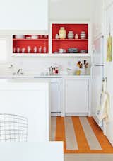 In the kitchen, Angle removed the cabinet doors and applied a coat of Poppy Red paint by Benjamin Moore, and put down a striped linoleum floor to brighten the space.