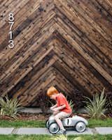 Passive House wood exterior with child riding toy car across grass lawn.