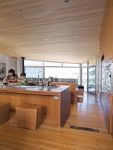 Lam and her son Max prepare a snack together in the open-plan kitchen at the center of the house. The fir floor that covers the living space steps downward twice, creating a grade change that roughly follows the topology of the site. The ceiling is sheathed in untreated hemlock; the custom stools were designed by Brent Comber.  Photo 5 of 9 in When Living on the Edge is Super Comfortable