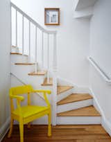 In the hallway, a yellow Raw chair by Jens Fager for Muuto pops against the white staircase.