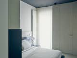 Bedroom, Bed, Wardrobe, Night Stands, Lamps, Storage, Concrete, and Shelves A custom lacquered-wood headboard with built-in task lights by MLE complements a Pianca bed in the master bedroom. An IC Lights T lamp by Michael Anastassiades for Flos offers additional illumination.  Bedroom Storage Bed Night Stands Concrete Photos from This Growing Family Maximizes Every Last Inch in Their 850-Square-Foot Apartment