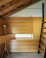 A custom ladder made of bent steel with oak treads leads to the sleeping loft, while a white oak panel swings opens to reveal an inset window. Longtime collaborator Jeffrey Kramer crafted the home’s wood elements.