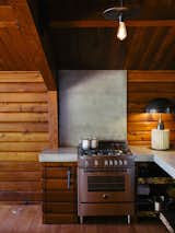 Kitchen, Wood Cabinet, Concrete Counter, Range, Ceiling Lighting, and Table Lighting A Column lamp by Apparatus and concrete countertops join a Bertazzoni propane range. The brass pendant is by Workstead.  Photos from An Eclectic Paciﬁc Northwest Cottage