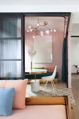 Glass partitions framed in powder-coated metal slide back to make flexible use of the floor plan in a 1,206-square-foot apartment, where color blocking the rooms also help break up the different spaces. The pink walls of the living room tie into the pink furniture in other rooms, keeping a sense of continuity while still differentiating between areas.