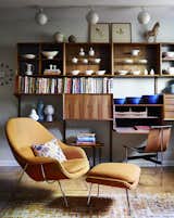 Illuminated by track lighting, a teak wall unit by Poul Cadovius showcases pottery by Eva Zeisel and Paul McCobb, among others. The desk seat is a T chair by William Katavolos, Ross Littell, and Douglas Kelley; the Womb chair is by Eero Saarinen for Knoll.