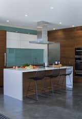 Kitchen, Range Hood, Wood Cabinet, Cooktops, and White Cabinet In the kitchen, a blue glass backsplash evokes the designers’ native Iceland. The  Bend Goods stools are from YLiving.  Photo 4 of 12 in A Southern Californian Prefab Is Paradise for the Whole Family