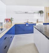 A wood countertop with blue laminate cabinets underneath contrasts with a white island topped with travertine. The wall tile is Origin Birch White by AKDO, and the brass faucet is by California Faucets. As in the rest of the apartment, the flooring is colored cork from Globus Cork.Photo by Mike Schwartz