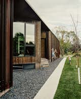 Beyond a bed of black granite rocks, an entrance is concealed in an alcove in the home’s cedar-and-weathered-steel facade. The windows were manufactured by Duxton Windows &amp; Doors.

East St. Paul, Manitoba
Dwell Magazine : November / December 2017