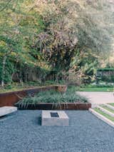 Outdoor, Garden, Gardens, Walkways, Concrete, Grass, Hardscapes, Shrubs, and Trees Behind her is the greenhouse, where Lynn starts vegetables like lettuce, Swiss chard, and tomatoes. Landscape architect David Hocker defined the sunken fire pit area with Cor-Ten steel.  Outdoor Concrete Walkways Gardens Garden Photos from A Black Stucco Home in Dallas Is Surrounded by Eye-Popping Greenery