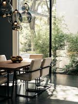 A table and chairs from Classic Home in the Dallas Market furnish the dining area. The chairs were upholstered by Berkeley Fabrics &amp; Upholstery. Lynn created the fixture overhead with hardware from Tech Lighting. “I never turn  on the lights during the day,” she says. “Even if it’s cloudy outside, there’s plenty of light in here.”  Photo 7 of 18 in A Black Stucco Home in Dallas Is Surrounded by Eye-Popping Greenery