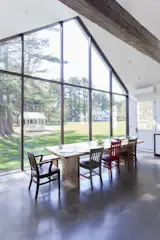 A cathedral-like kitchen features polished heated concrete floors and a two-story wall of skyscraper glass framing views of the water, gazebo, apple trees, and historic barn.