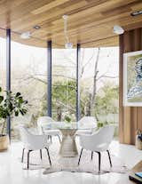 Dining, Table, Rug, Ceiling, Chair, Recessed, and Terrazzo Because the property slopes to the rear, the home’s eastern view is of treetops right outside. In the dining nook, Executive Armchairs by Eero Saarinen join a Warren Platner table beneath a Serge Mouille ceiling light. A patterned rug by AVO rests on the terrazzo tile floor.  Dining Ceiling Terrazzo Table Photos from This House in Austin Has a Tree Growing Right Through It