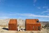 Surrounded by boulders and twisted yuccas, these two cabins in the Mojave Desert stand like Monopoly houses, with their steel siding weathered to a tawny finish. But behind the simple gabled forms lies a complex network that enables them to operate wholly off the grid.&nbsp;