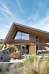 Outdoor, Shrubs, Walkways, Large Patio, Porch, Deck, Concrete Fences, Wall, and Back Yard On a scenic but exposed lakefront site on New Zealand’s South Island, architects Tim Lovell and Ana O’Connell of Lo’CA created a pitch-roofed 2,690-square-foot residence for Tim’s parents. The home’s courtyard was excavated to help shelter it from high winds. A 10-foot eave over the windows and doors assists with sun shade and heat retention during the intense summer and winter months.  Photo 1 of 9 in This Bunker-Like Home in New Zealand Fights Back Against Howling Winds Off Lake Wanaka