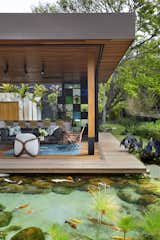 Outdoor, Wood, Back Yard, Small, Horizontal, Trees, Grass, Shrubs, and Boulders The home appears to float above the natural pool, adding an element of whimsy.  Outdoor Small Wood Grass Photos from This Breezy Brazilian Home Oozes Tropical Vibes