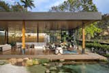 Outdoor, Trees, Horizontal, Boulders, Shrubs, Small, Back Yard, Grass, and Wood Beyond the living room and deck, a natural pool filled with koi fish serves as a unique focal point of the tropical garden.  Outdoor Trees Horizontal Small Photos from This Breezy Brazilian Home Oozes Tropical Vibes