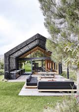 A blackened-timber pergola extends from the modern barn that architect Greg Scott designed for Jody and Deirdre Aufrichtig in the Elgin Valley, an apple- and grape-growing region near Cape Town. Made of narrow slats stabilized with randomly scattered blocks of wood, it  covers roughly half of the outdoor deck.