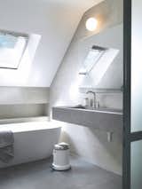A skylight allows natural light to flow over the freestanding tub. The taps, soap dispenser, and pedal bin are by Vipp.