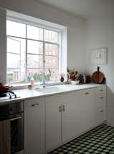 Kitchen, White Cabinet, Ceramic Tile Floor, Drop In Sink, Dishwasher, and Engineered Quartz Counter This compact Brooklyn kitchen features a white Corian counter and integrated sink, IKEA cabinets with custom pulls, and geometric floor tiles in black, white and green from a collaborative series by Heath and Dwell. Black appliances pull the look together nicely.  Photo 6 of 17 in Two Magazine Creatives Fit Graphic Art and Vintage Furniture in a Brooklyn Apartment