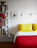 Bedroom, Medium Hardwood, Bookcase, Wall, and Bed Even the bedding adheres to the color scheme, with yellow pillows from Merci in Paris and a red blanket from Best Made. The sconce is by David Weeks Studio.  Bedroom Wall Bed Bookcase Medium Hardwood Photos from Two Magazine Creatives Fit Graphic Art and Vintage Furniture in a Brooklyn Apartment