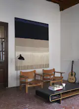 The living room also includes a pair of Spanish chairs by Børge Mogensen, a vintage floor lamp, and a painting by Kate Blee. A guitar, made by Chris, rests on the ceramic tile floor.