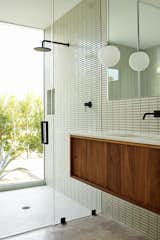 Bath, Concrete, Drop In, Enclosed, Pendant, Accent, Glass Tile, and Full New plantings provide privacy for the glass-walled shower in the master bathroom. The matte black fixtures are by Phoenix.   Bath Concrete Drop In Enclosed Accent Photos from Ex Alt-Rockers Revive a Midcentury Gem Near Palm Springs—and Find it May Be a Lost Masterpiece