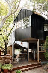 Outdoor, Trees, Wood, Gardens, Back Yard, and Shrubs Working around mature eucalyptus and elm trees, architect Murray Barker sited a new home for Fleur Glenn on her property in Clifton Hill, Australia. The trees also drove the home’s shape, with angles meeting the gabled roof in unexpected ways. The south elevation mixes black-stained timber and cement board with board-and-batten siding.  Outdoor Trees Shrubs Gardens Wood Photos from This Light-Filled Bungalow Exudes Playful Tree House Vibes