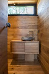 The wood-clad bathroom features a full shower and custom-made natural stone sink, which was created from a rock found at a neighboring river.&nbsp;