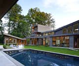Outdoor, Walkways, Trees, Back Yard, Rooftop, Large Pools, Tubs, Shower, Concrete Pools, Tubs, Shower, Concrete Patio, Porch, Deck, Slope, Grass, Shrubs, Hardscapes, Landscape Lighting, and Swimming Pools, Tubs, Shower From the rear, the home’s layout as a two-story structure becomes clearer, as does its aggressive use of angular dimensions and expansive walls of glass.  Photo 1 of 9 in Walls of Windows Connect a Home With Earth and Sky