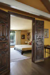 While public areas utilize brighter colors inspired by Venetian sunsets, the bedroom, through these carved mahogany doors, is a space of softer tones and textures.