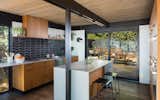 An open kitchen was rebuilt to face the rear courtyard. Contemporary features include a pop of color contrasting with teak veneer cabinetry and other wood tones.