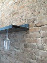 I-beam flanges echoing the dimensions of a wine glass were welded together to create the wineglass rack; the industrial material strengthens the raw look of the exposed brick.