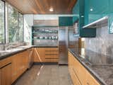 In the newly remodeled kitchen, teal-colored upper cabinetry adds a playful touch of color, contrasting with a more neutral palette of wood, granite, and stainless-steel.
