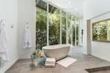 A serene, spa-like master bathroom features a stand-alone soaking tub and a wall of glass overlooking a private garden. The bathroom is one of two attached to the suite.