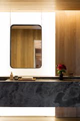 A look at a guest bathroom. The floating stone vanity is juxtaposed against wood panels and a backlit feature wall.
