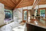 A look at the master bathroom, which features custom tile design, copper sinks, and marble countertops. The glass shower overlooks a view of the garden from a large picture window.