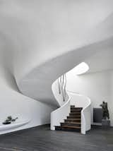 A sweeping staircase spirals up to the second floor. A sculpture plays off the black marble floors, and a bonsai perches preciously on a rounded display ledge.