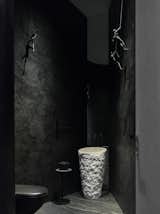 Dark figurines rappel from the ceiling in the black, sun-dappled bathroom.&nbsp;