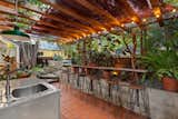 Another lush patio area just off the kitchen offers a pergola-topped outdoor kitchen and bar. Other features of the backyard include a&nbsp;fire pit, raised-bed gardens, and matured fruit trees.