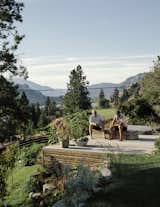 Outdoor, Back Yard, Flowers, Wood Patio, Porch, Deck, Shrubs, and Trees Vallely and Craig take in the sun on the raised deck in the backyard.  Photos from This Handcrafted Home in British Columbia Has Joyful Camp Vibes