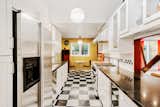 The updated galley kitchen mixes retro style with modern amenities. A black-and-white checkered pattern lines the floor, complementing the cabinetry and quartz counters. A pass-through connects looks into the living and dining area.