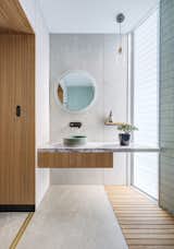 In one of the home's bathrooms, a sink from Lindsey Wherrett Ceramics gracefully sits under a circular mirror from Clearlight Designs. The Ilde Wood S pendant is by David Abad.